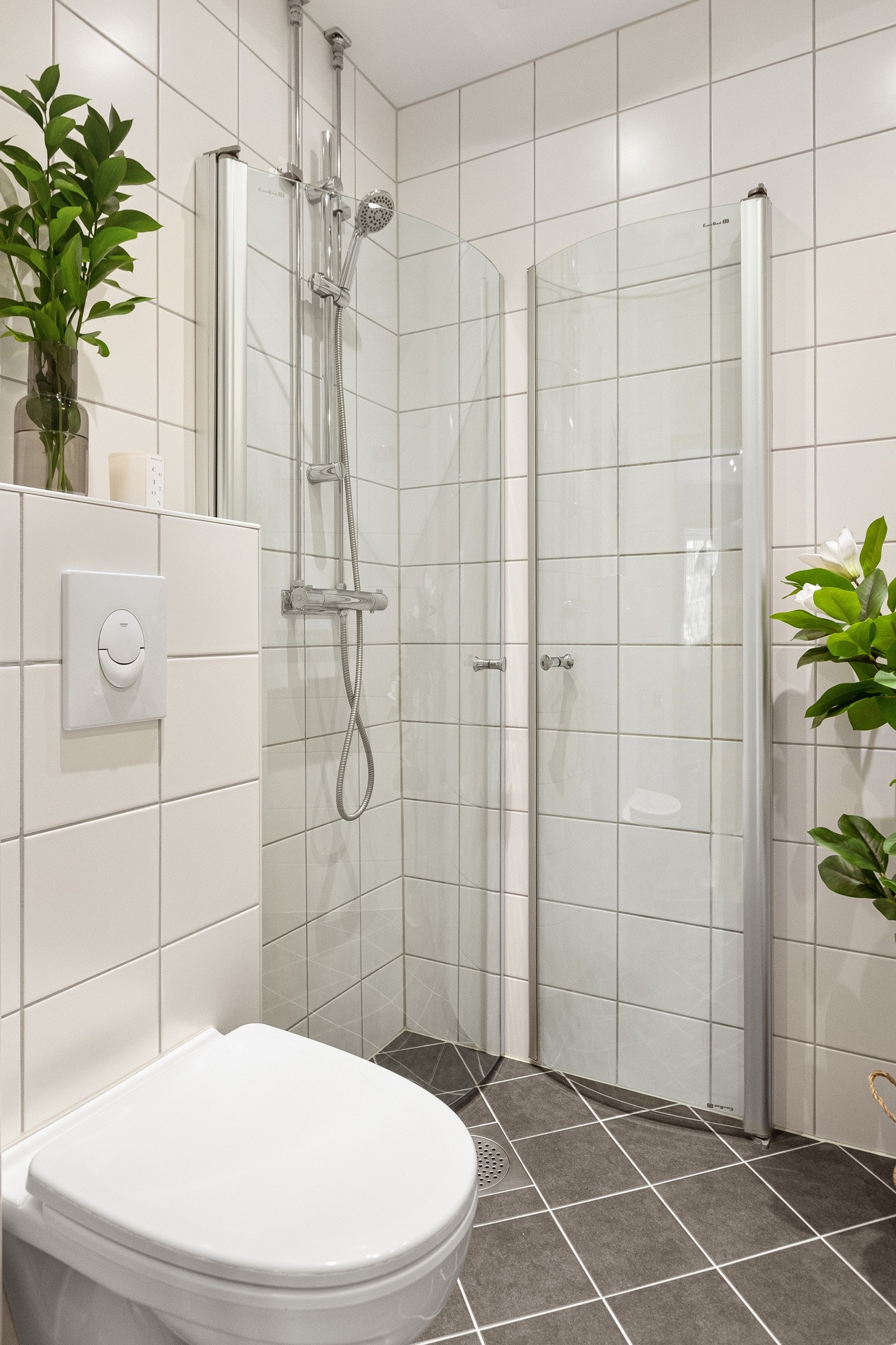 Baderommet inneholder servantskap og speilskap, opplegg for vaskemaskin (smal type), veggmontert klosett, samt dusjhjørne med buede svingdører. Galleribilde