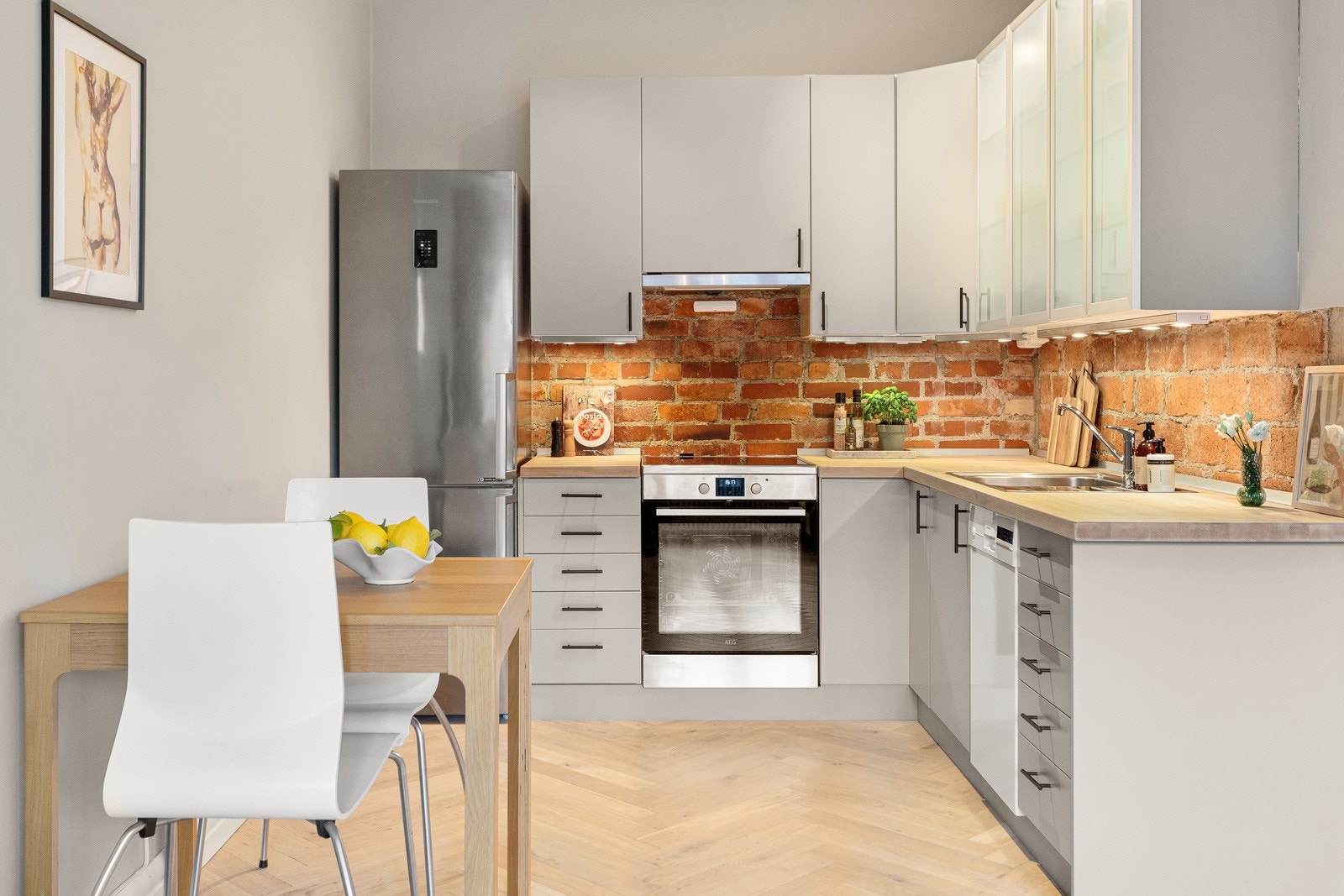 Her har du benkeplate i heltre med nedfelt kum i rustfritt stål, tiltalende innredning med malte fronter, samt sjarmerende tegl mellom over/underskap. Galleribilde