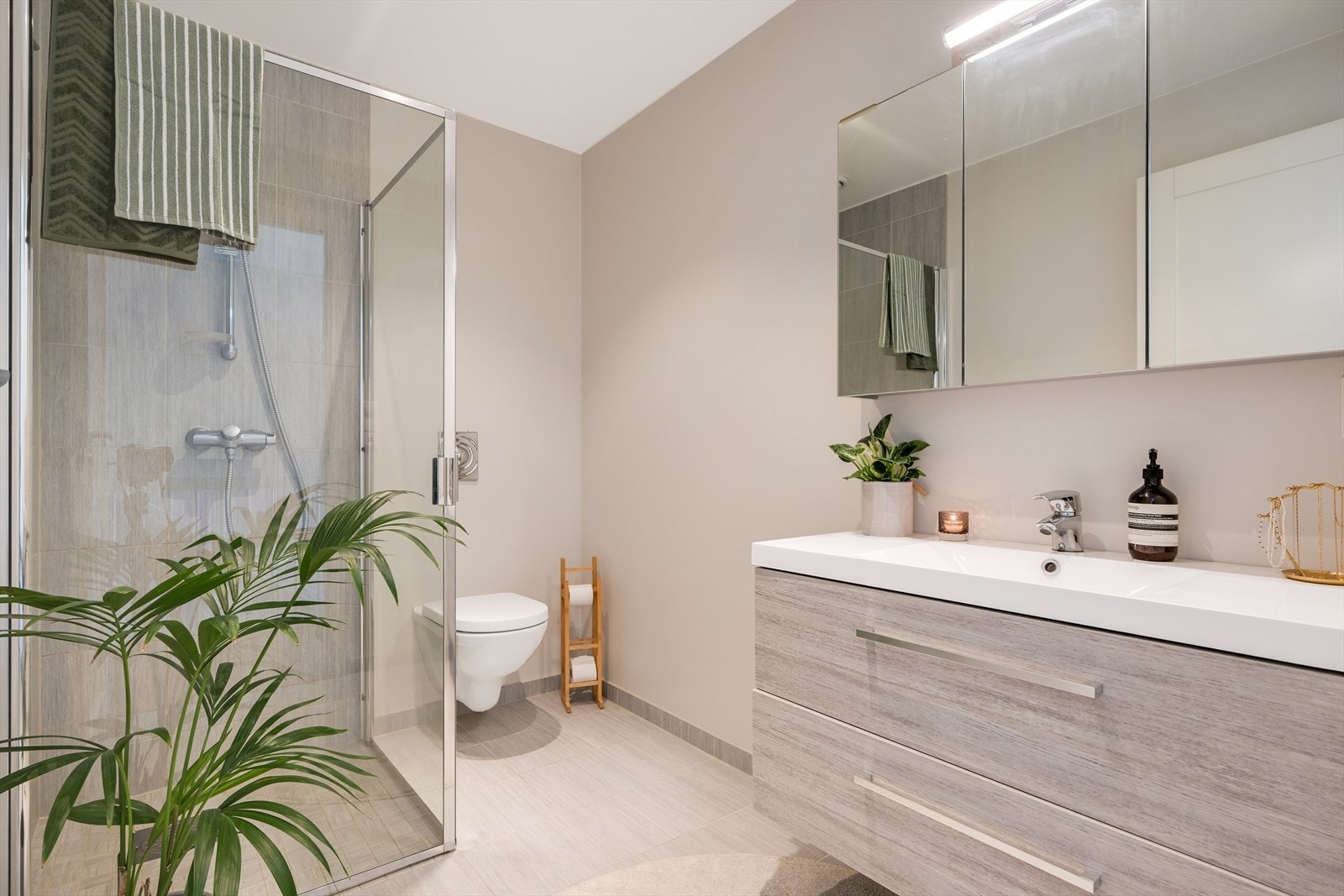 Bad/wc i 2. etg med fliselagt gulv og fliser i dusj. Vegghengt toalett og servant i innredning med skuffer, speilskap. Galleribilde