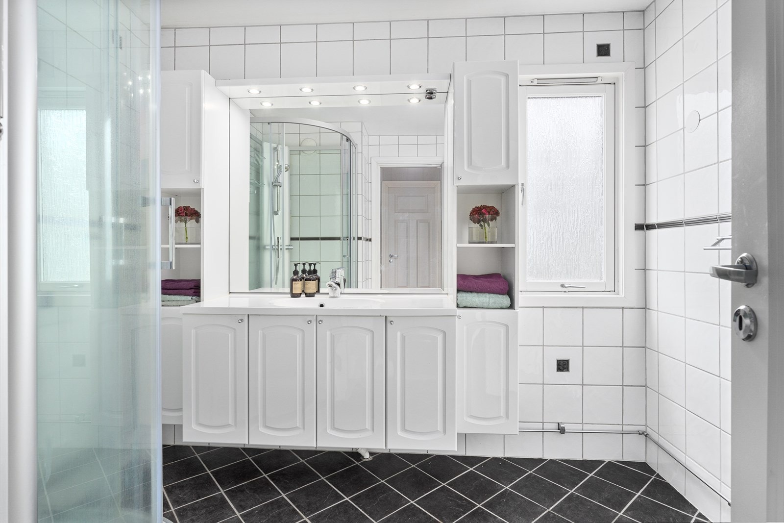 Pent flislagt bad med gulvvarme. Utstyrt med dusjkabinett og romslig baderomsinnredning med mye oppbevaringsplass. Det er også opplegg for vaskemaskin. Galleribilde