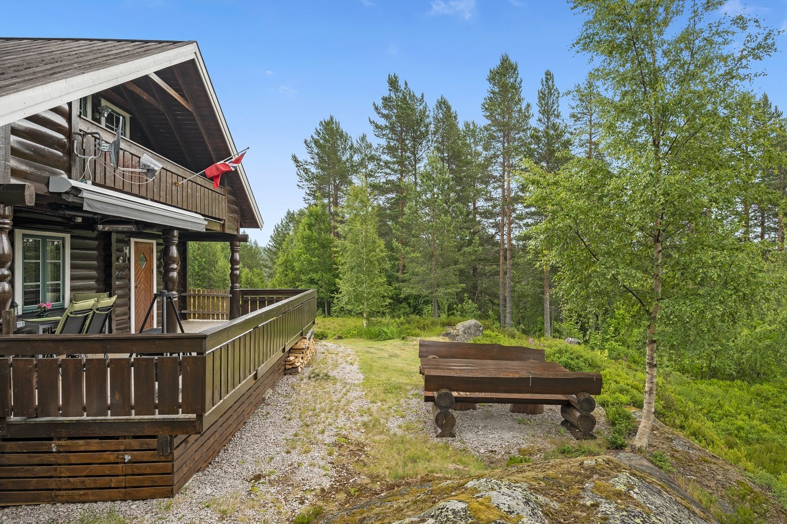 Utearealet rundt hytta har grus, gress, blomster, trær og annen stedlig vegetasjon. Galleribilde