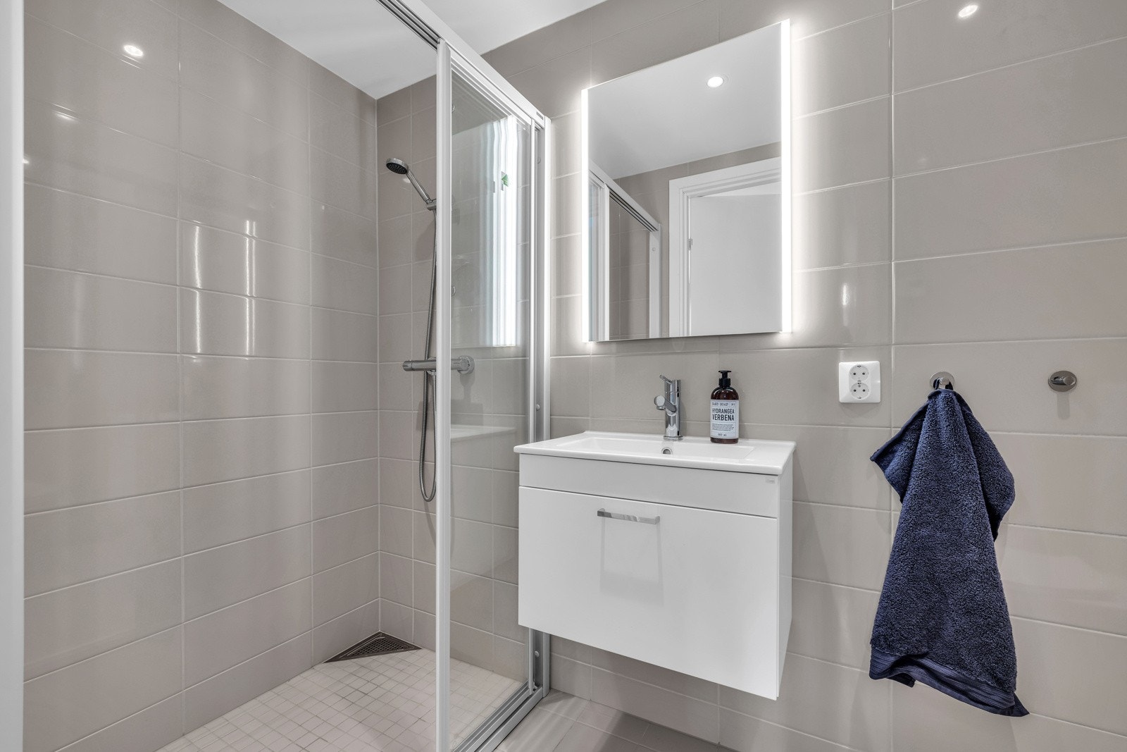 Baderommet har beige fliser, varme i gulvet og en romlig dusj nisje med glassdør. Galleribilde