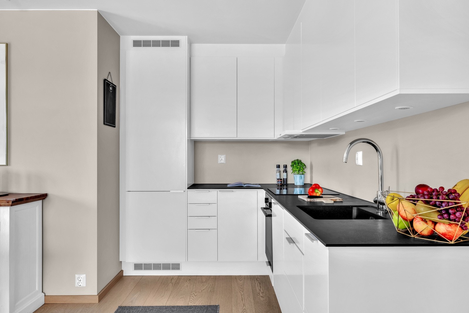 Lys kjøkkeninnredning med glatte fronter, benkeplater i laminat, oppvaskkum med ett-greps blandebatteri og ventilator over kokesonen tilkoblet fellesanlegg. Galleribilde