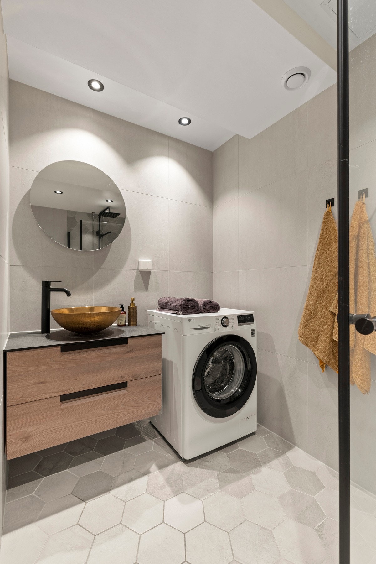 Innredningen inkluderer en servant med slette fronter, veggmontert toalett, dusjhjørne med to svingbare glassdører og opplegg for vaskemaskin Galleribilde