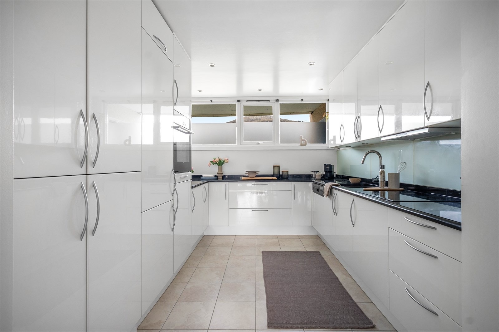 Flott kjøkken fra Mobalpa som er innredet med hvite høyglansfronter og benkeplate i stein. Galleribilde