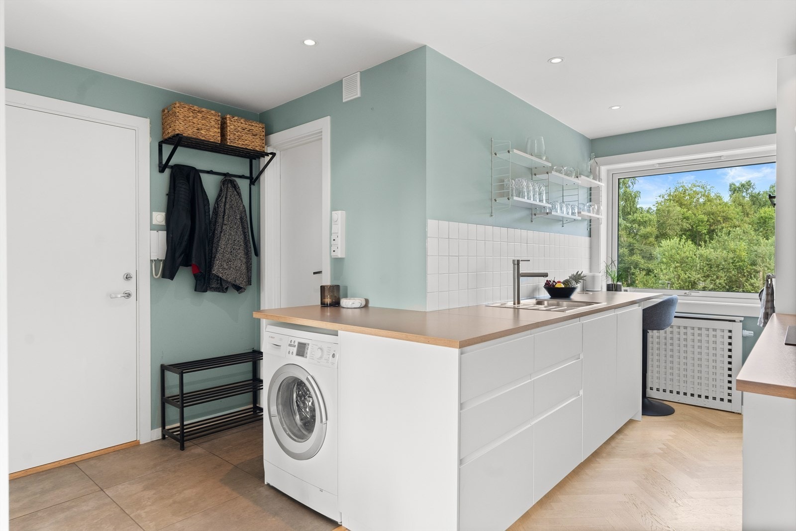 Laminert benkeplate med nedfelt vaskekum og fliser over kjøkkenbenk. Kjøkkenet har ventilator, integrert oppvaskmaskin, komfyr, mikro, topp og kjøleskap Galleribilde