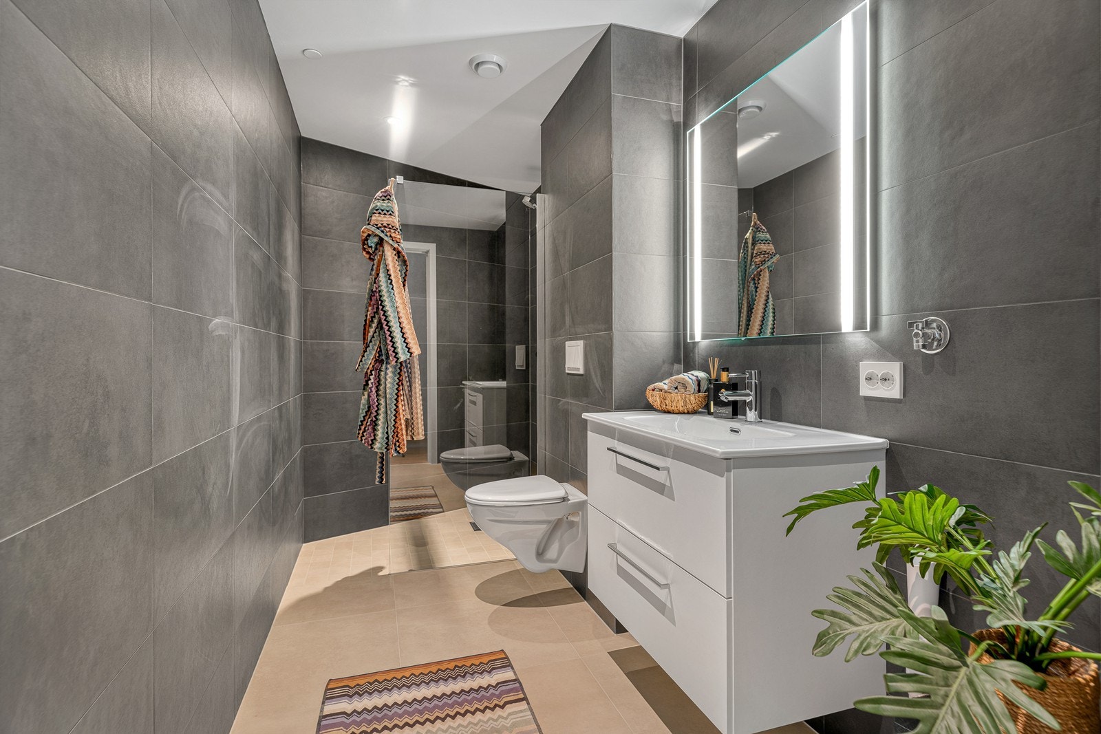 Leilighetens andre bad er bevart i samme gjennomførte stil, med flislagte overflater og behagelige varmekabler i gulvet Galleribilde