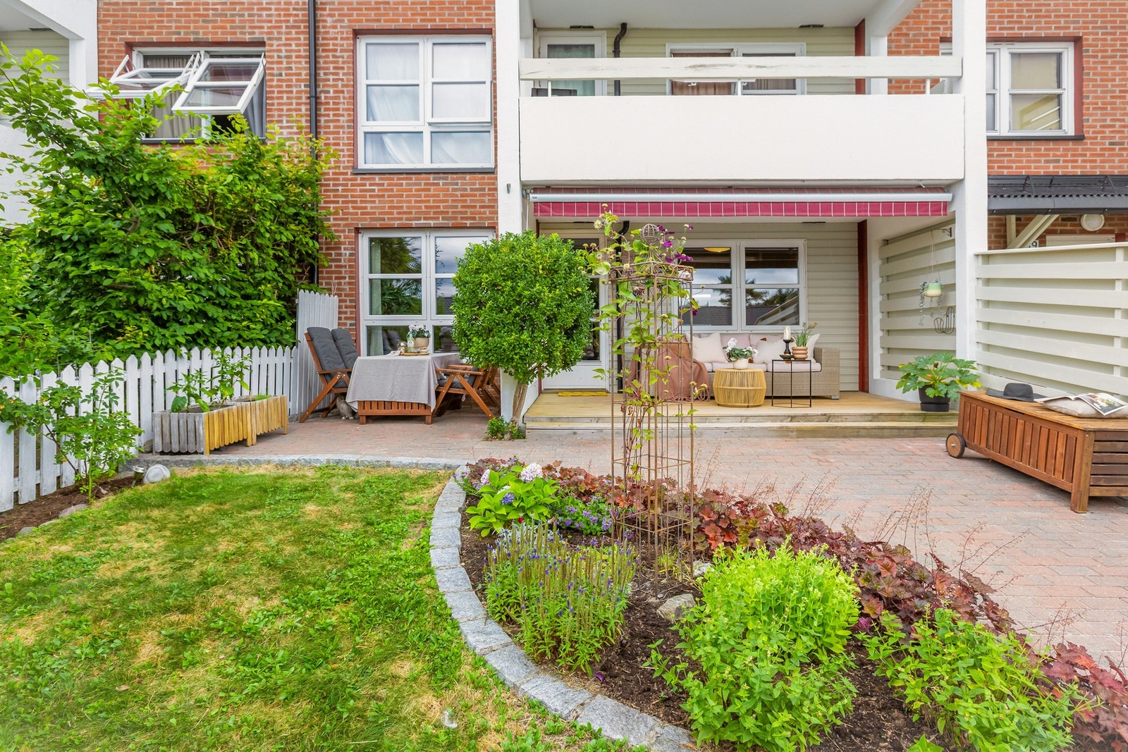 Fra stuen kommer du ut til denne private, flotte og solrike uteplassen som byr på terrasse, sjarmerende brostein, frodig gressplen og vakker beplantning. Galleribilde