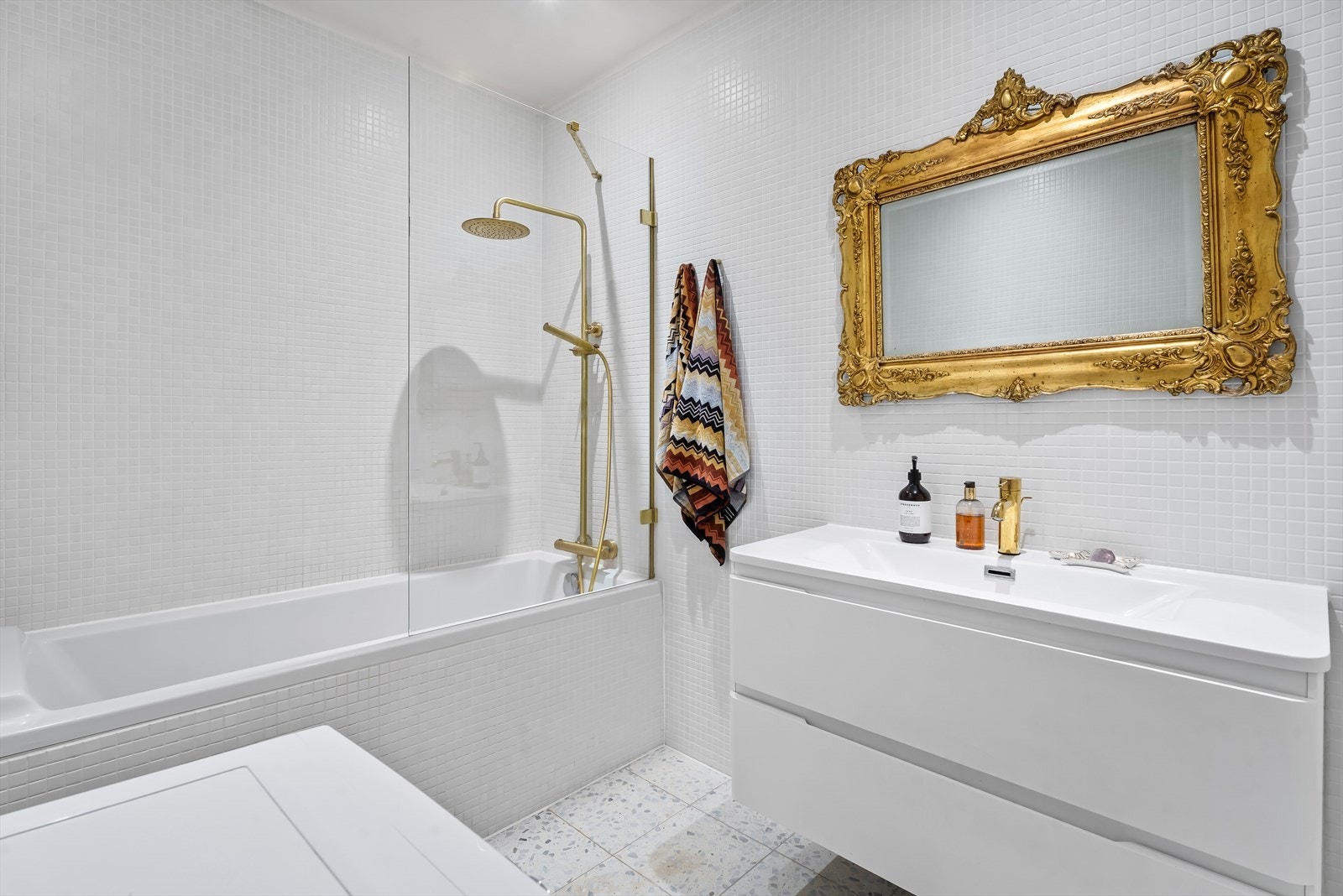 Badet er innredet med heldekkende servant på underskap, speil med belysning, vegghengt toalett og dusjløsning i badekar Galleribilde