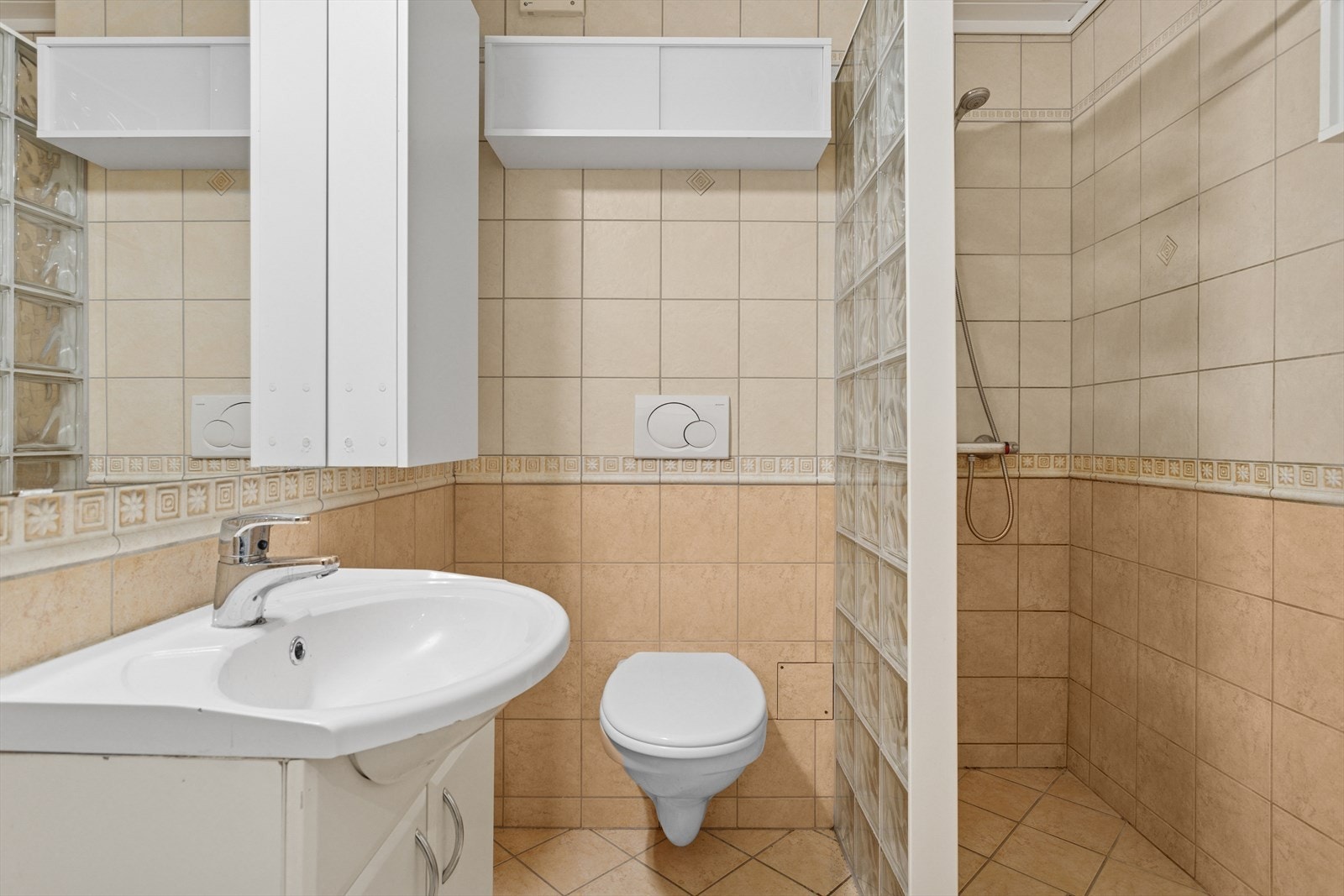 Flislagt baderom med gulvvarme, dusjhjørne, oppbevaring i baderomsmøbler og vegghengt klosett. Galleribilde