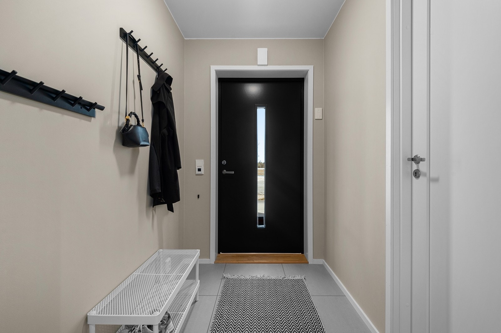 Ta av deg skoene og heng av deg jakken før du tar turen videre i ditt nye hjem. Fliser med varmekabler i gulv og oppheng for ytterklær på vegg. Galleribilde