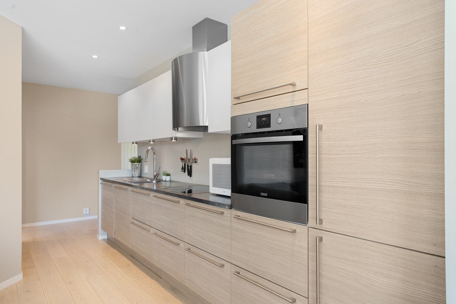 Tiltalende HTH kjøkken med eikefronter på underslag og høyskap og hvite overskap - det er integrerte hvitevarer og Røroshetta ventilator i stål Galleribilde