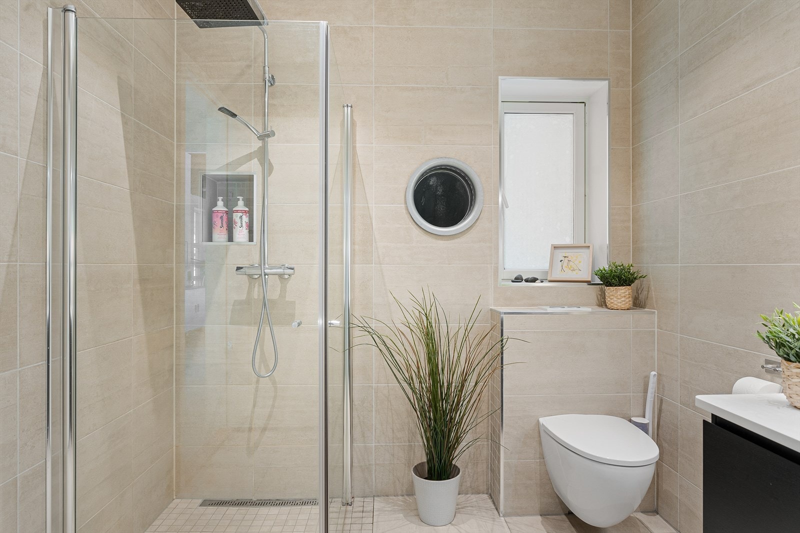 Badet er innredet med vegghengt toalett, moderne baderomsinnredning med skuffer samt dusjnisje med glassdører Galleribilde