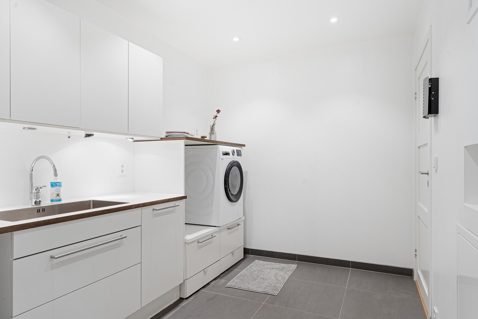 Stort vaskerom med kjekk innredning med skuffer, vask, overskap og vaskerom/tørketrommel i praktisk høyde Galleribilde