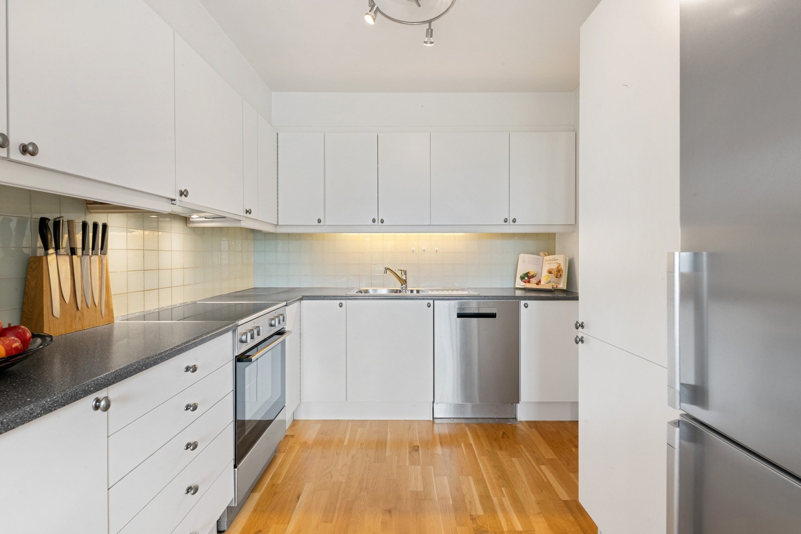 Praktisk kjøkkeninnredning utstyrt med kjøle-/fryseskap, oppvaskmaskin og komfyr Galleribilde