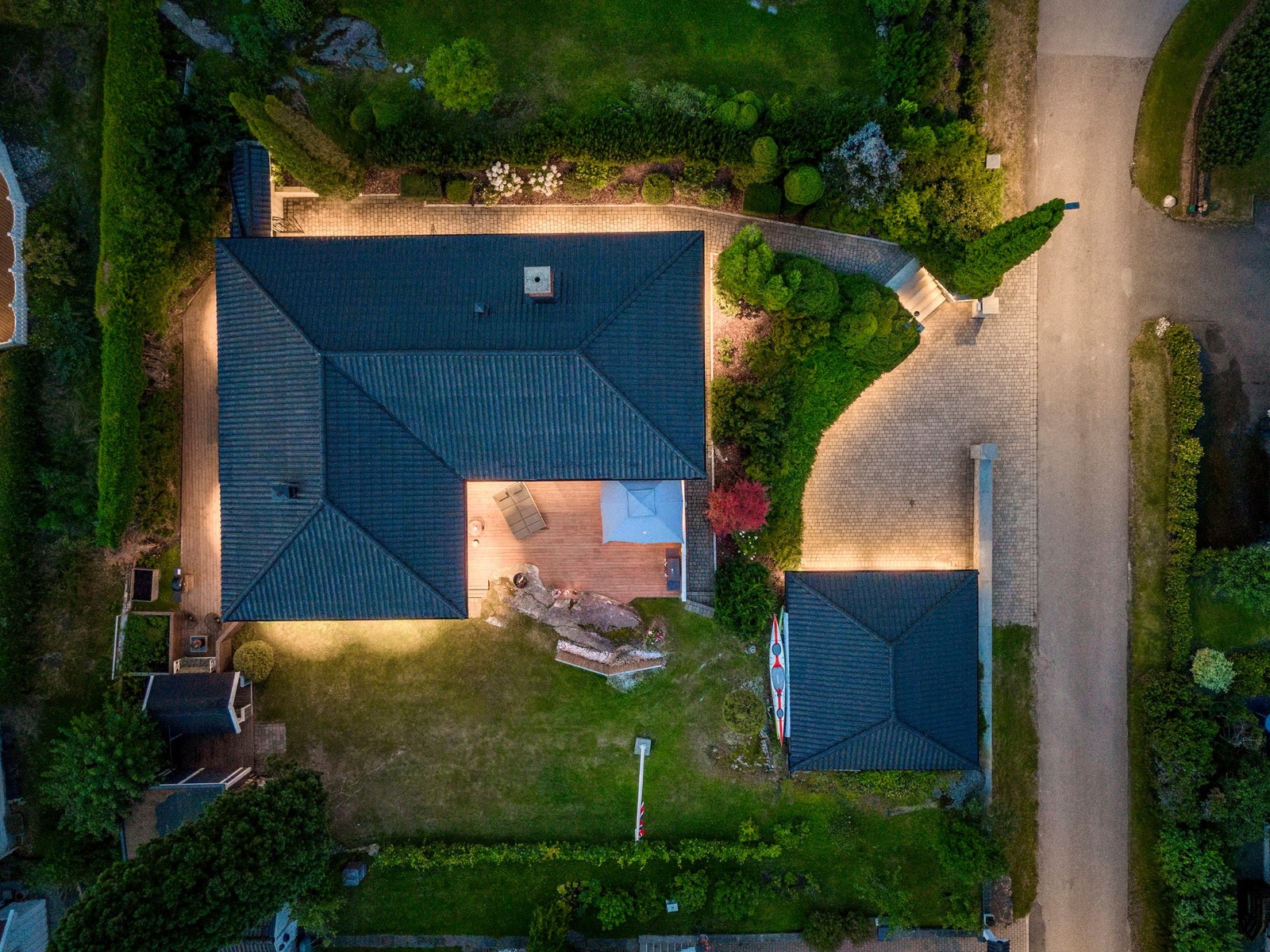 Fra gårdsplassen fører en steintrapp opp til inngangspartiet på østsiden av huset. Det er montert godt med utebelysning langs gangarealet og alle sider av fasaden. Mot hagen i sydvest er det anlagt en stor markterrasse fra 2021 med utmerkede solforhold. L Galleribilde