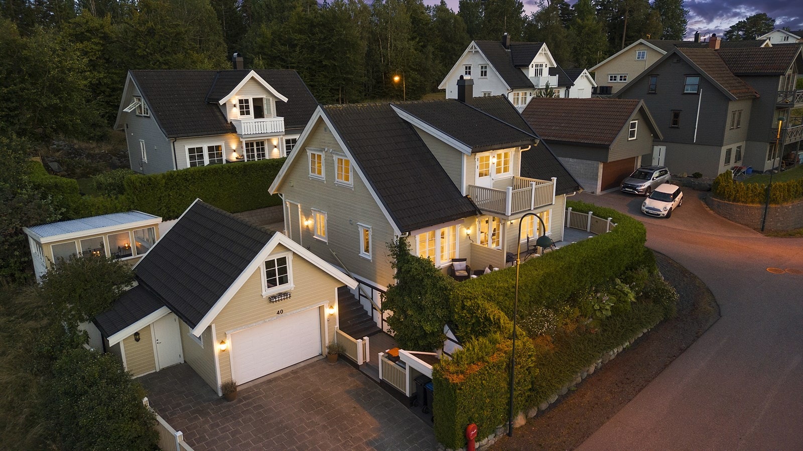 Kveldsstemning som viser bebyggelsen på tomten med eneboligen, garasjen, utebod samt utestue. Galleribilde