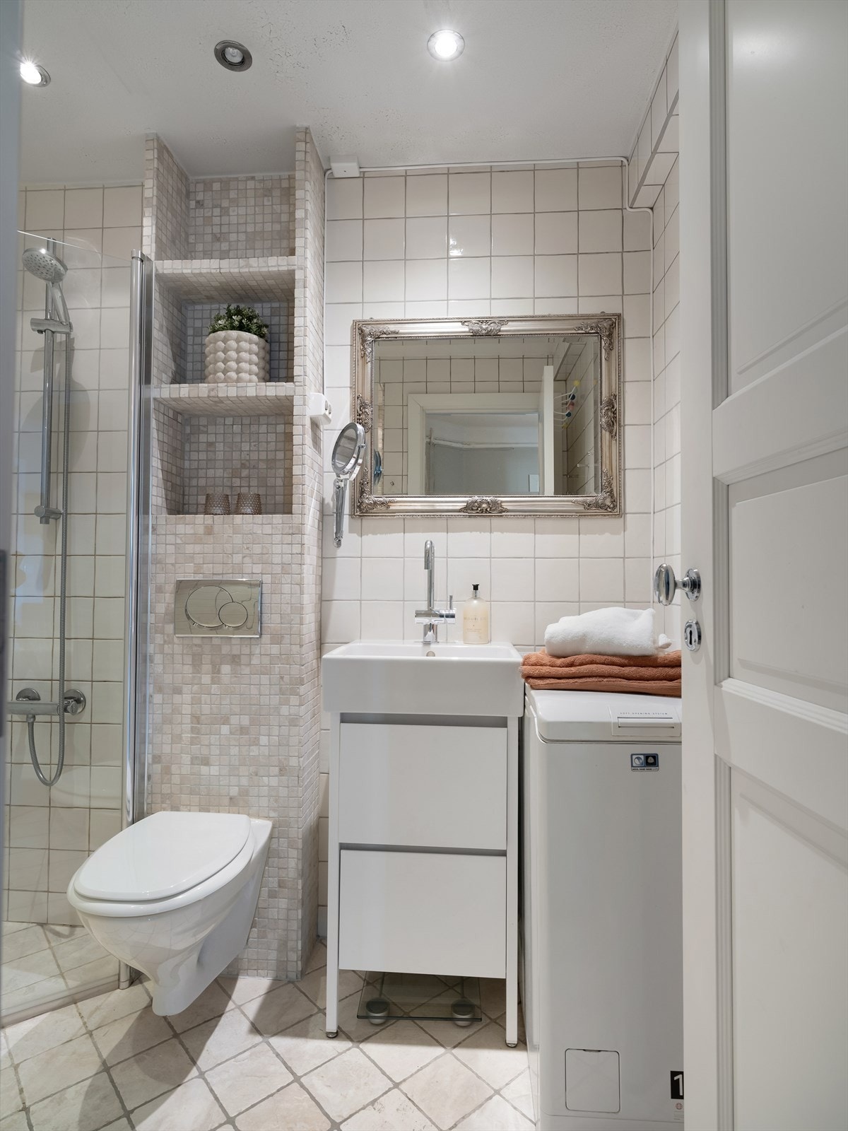 Badet er utstyrt med dusjhjørne, innfellbare dusjdører, mekanisk avtrekk, stoppekran og veggmontert wc. Opplegg for smal vaskemaskin Galleribilde
