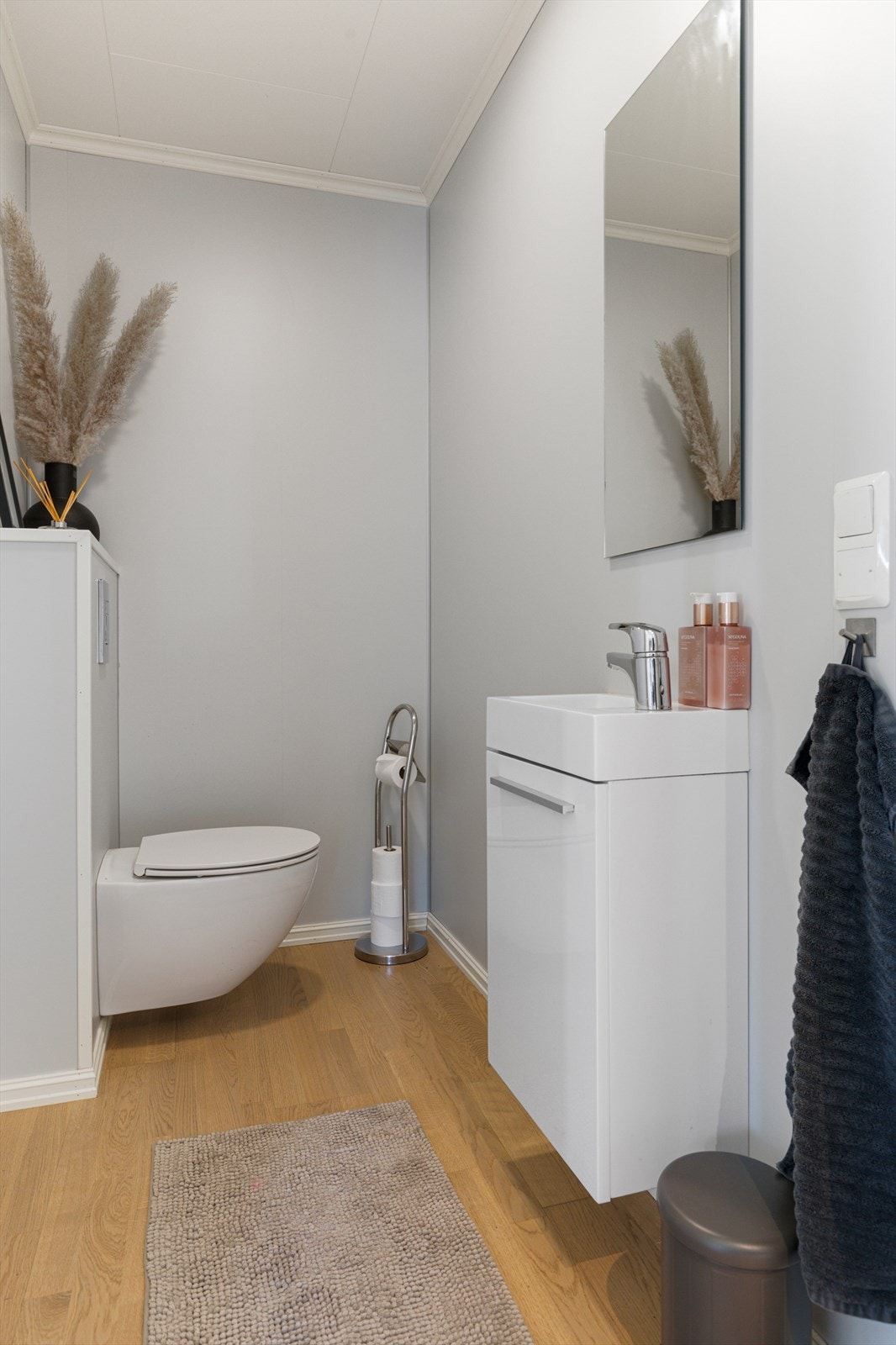 Toalettrom med parkett på gulv og tapetserte/malte vegger. Innredet med servantskap og vegghengt toalett. Galleribilde