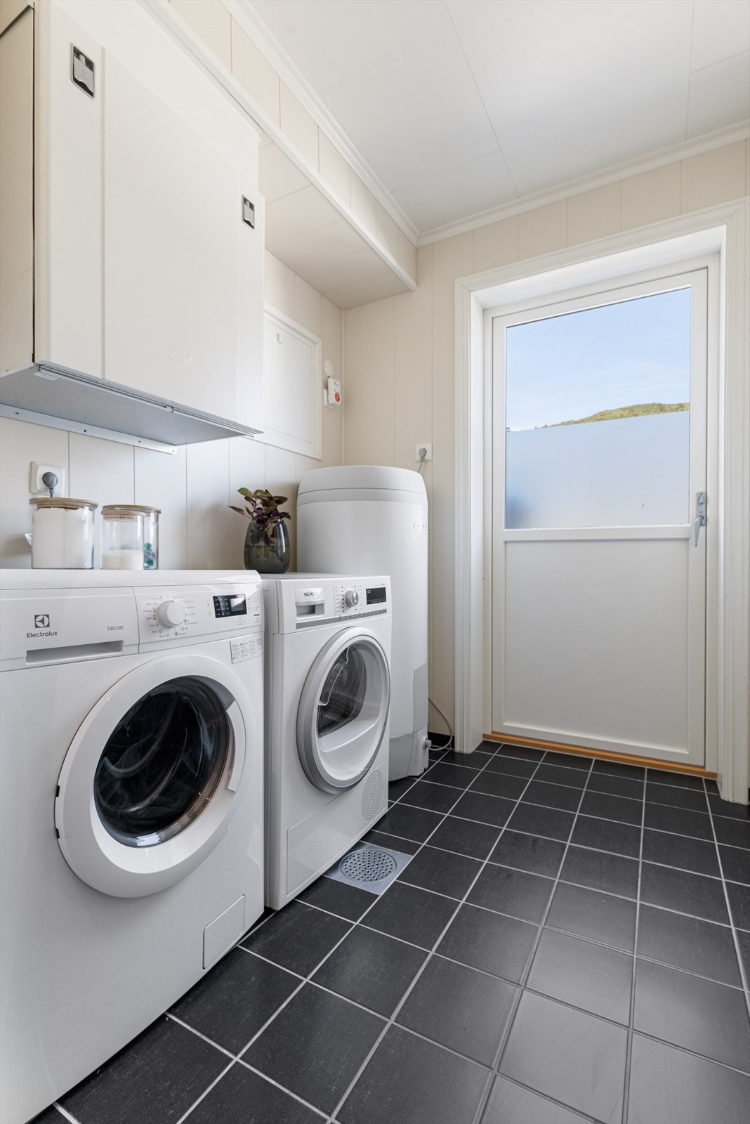 Vaskerom med flislagt gulv og sokkelflis, samt plastsluk og ca. 30 mm fall. Rommet har smartpanel på vegger og inneholder blant annet varmtvannsbereder, sikringsskap, ventilasjonsaggregat og opplegg for vaskemaskin. Galleribilde