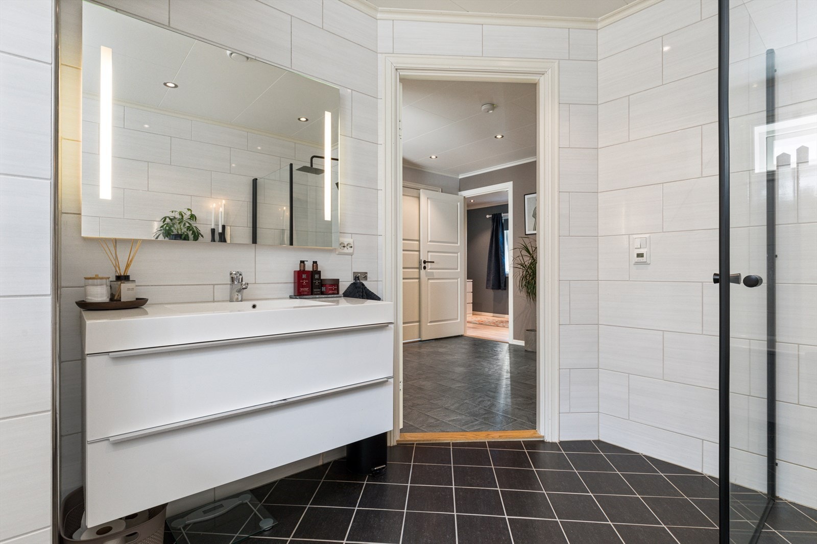 Badet har flislagte overflater, LED-downlights i himlingsplater og elektriske varmekabler i gulv. Utstyrt med heldekkende servant, veggmontert toalett, badekar og dusjhjørne. Galleribilde