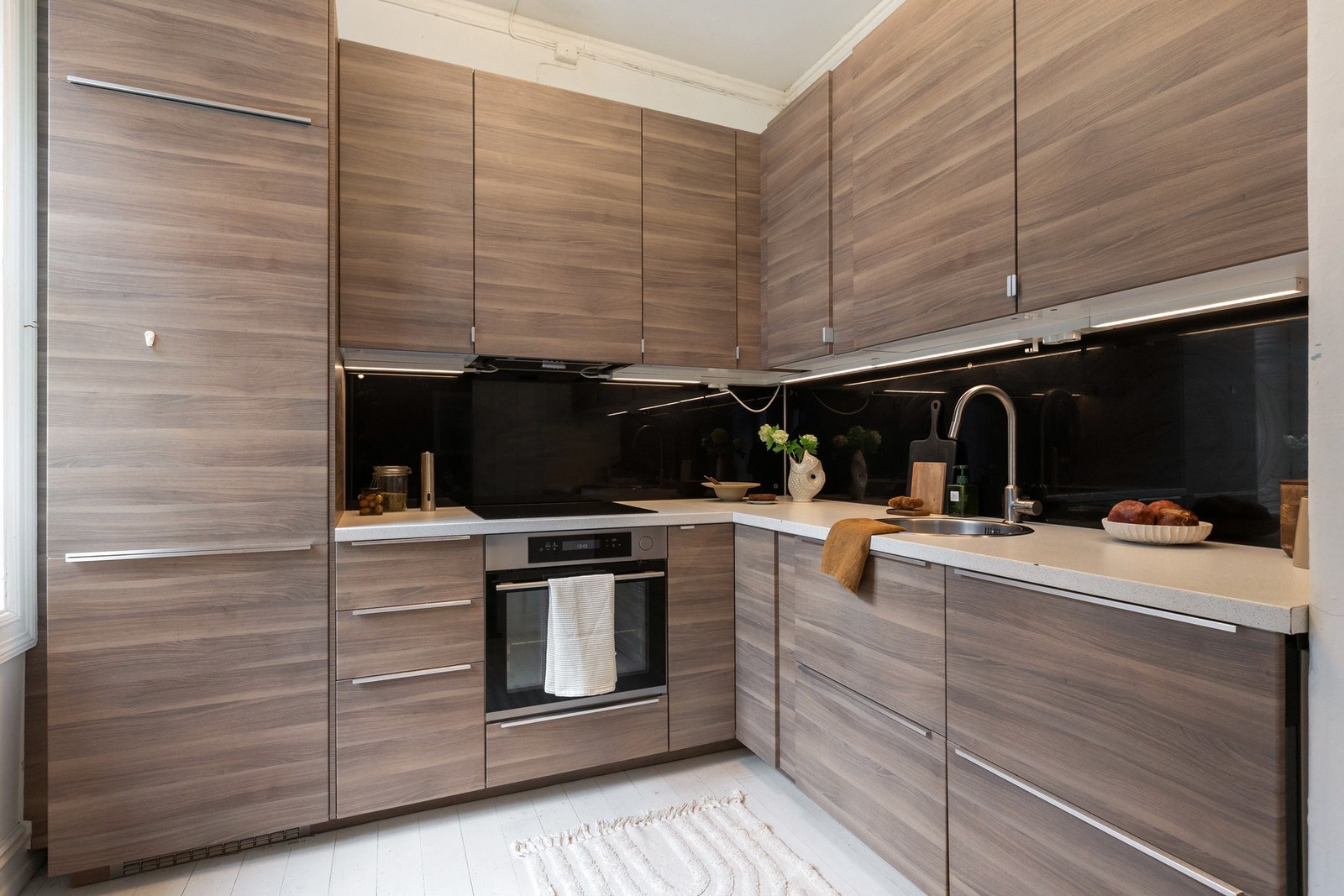 Kjøkkeninnredningen er utstyrt med glatte fronter og laminat benkeplate. Det er glassplater på vegg over benkeskap, noe som bidrar til enkel rengjøring. Galleribilde