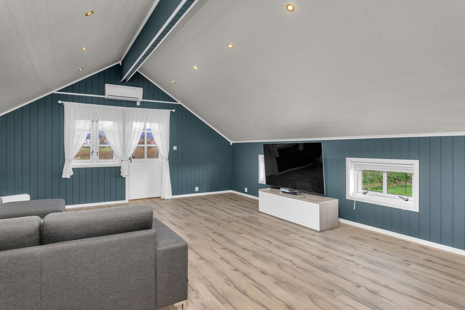 TV-stuen har en lun atmosfære med blågrønne vegger, spotter i taket og oppvarming med varmepumpe. Galleribilde