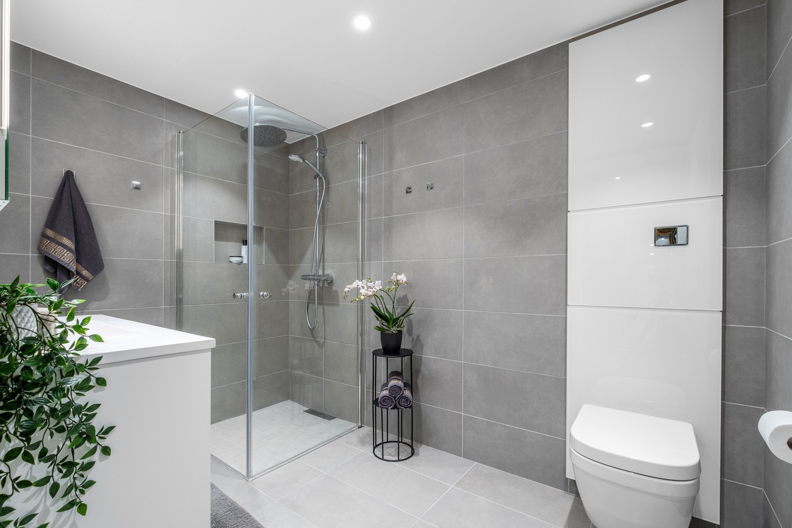 Flislagt baderom på 5,5 kvadratmeter med innfellbare dusjdører og vegghengt toalett. Galleribilde