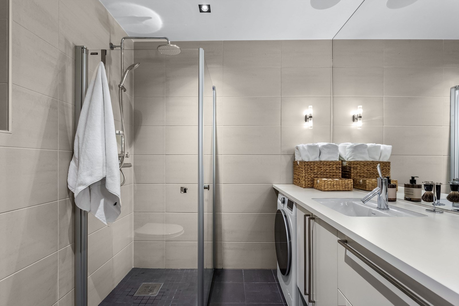 Delikat og innbydende bad med stor dusjsone, gulvvarme, downlights og servant med bred overbenk Galleribilde