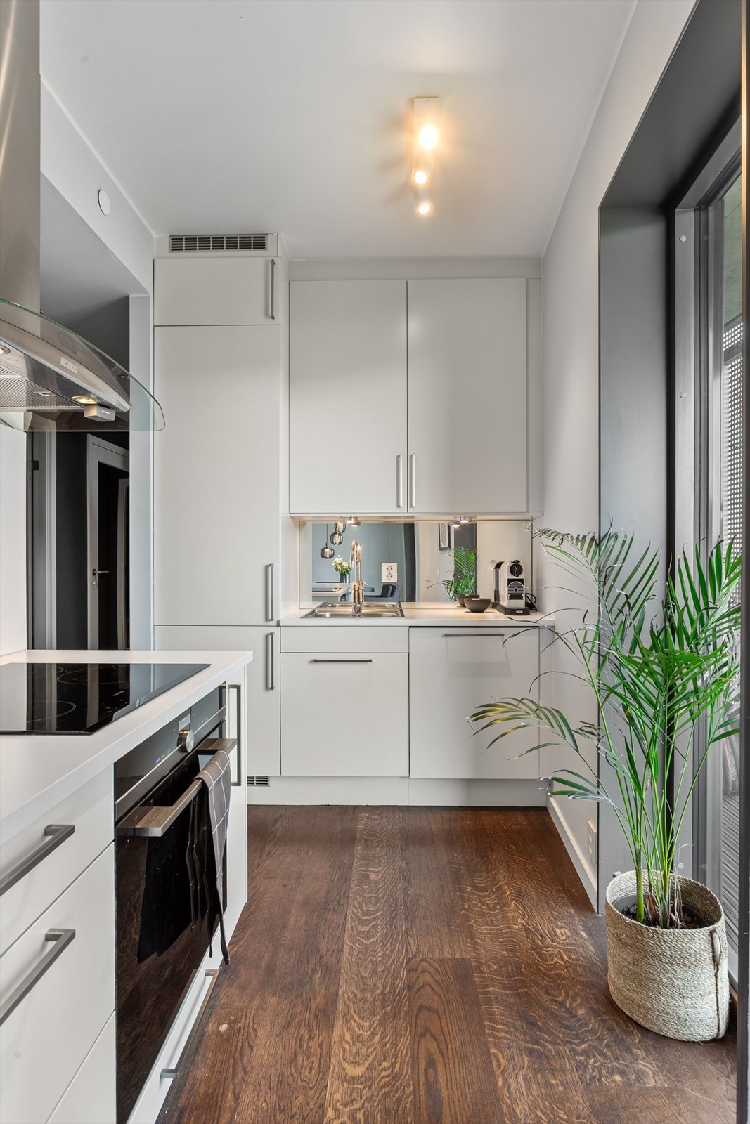 Lys og pen kjøkkeninnredning med bla. speil splashback og integrerte hvitevarer Galleribilde