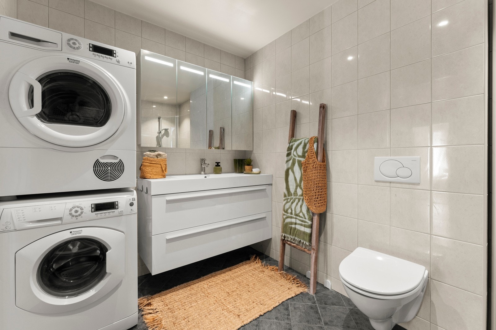 Badet er både lekkert og praktisk, med flotte fliser på gulv og vegger, samt gulvvarme for ekstra komfort. Det er romslig og godt utnyttet, med plass til både oppvaskmaskin og tørketrommel i søyle. Galleribilde