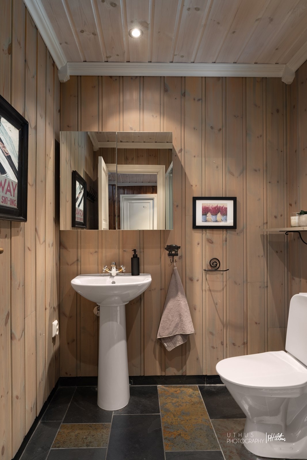 Det er et praktisk baderom ved entreen som har fliset gulv med varmekabler og beiset panel på veggene Galleribilde