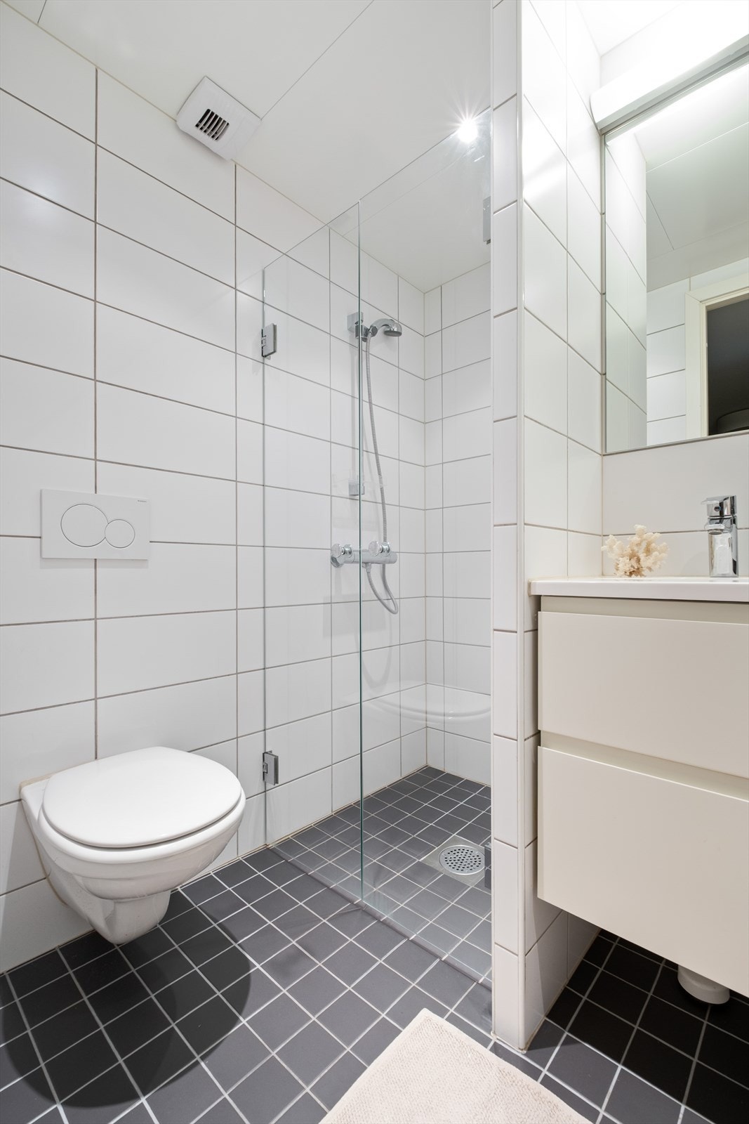 Badet er innredet med vegghengt klosett, servant nedfelt i innredning og dusjhjørne med svingbare glassdører. Galleribilde