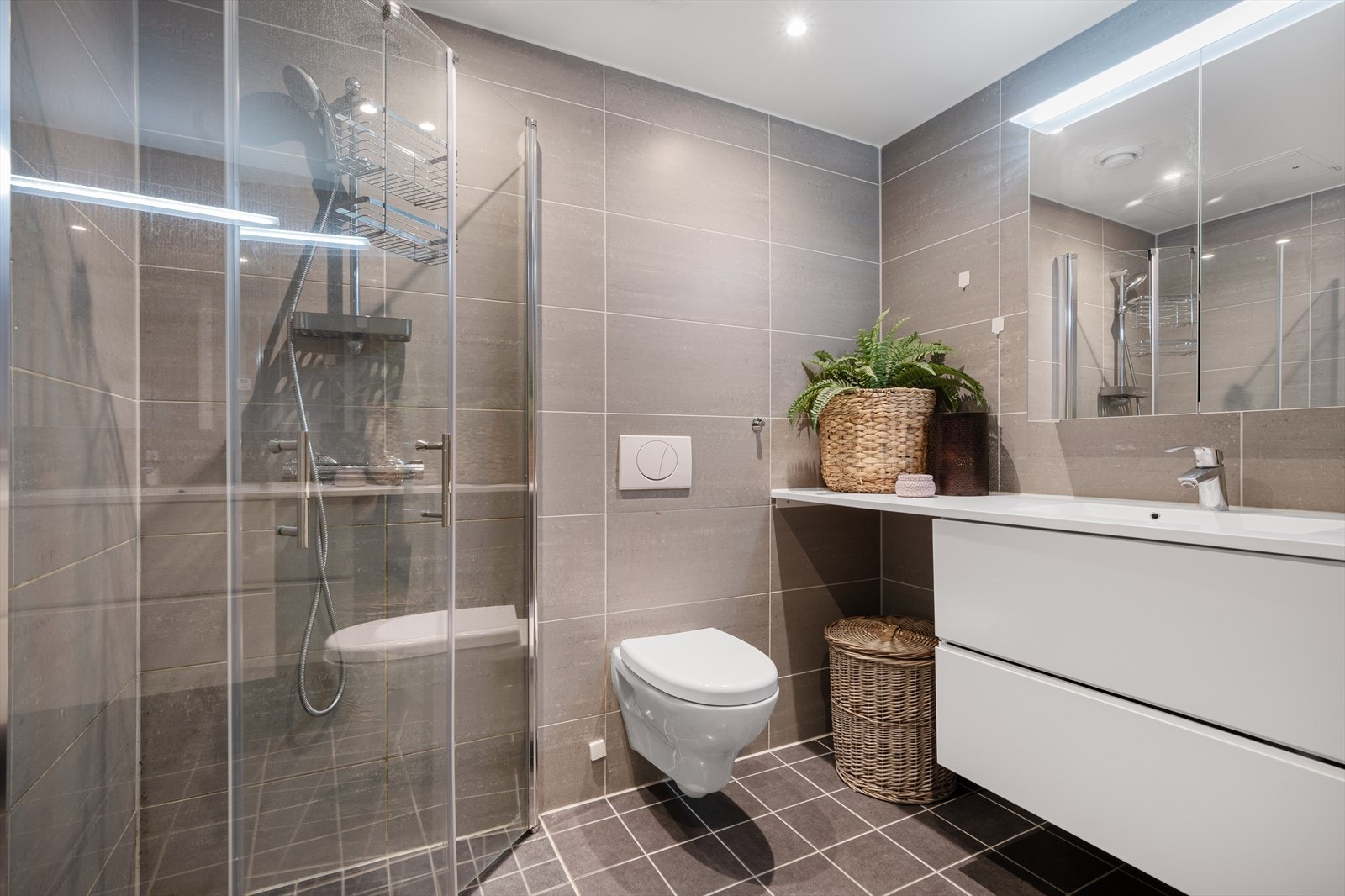 Badet er innredet med vegghengt toalett, servant på skuffeseksjon, speilskap med belysning, dusjhjørne og opplegg for vaskemaskin. Galleribilde