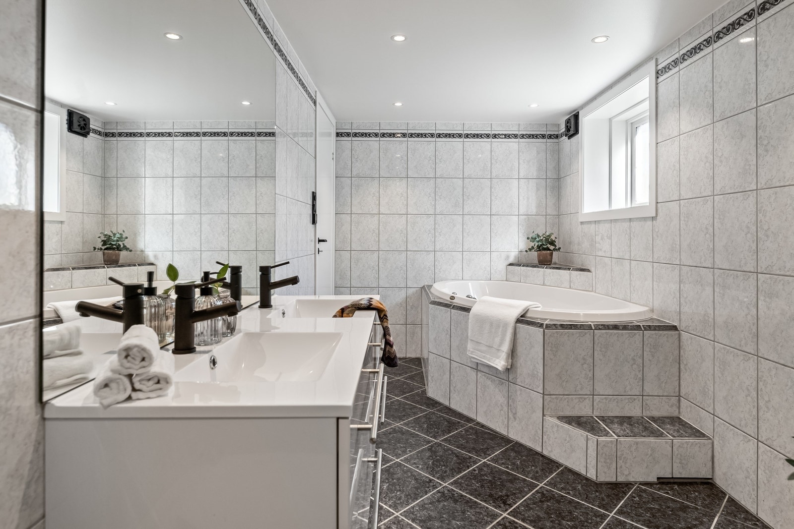 Badet inneholder innredning med to nedfelte servanter, veggmontert toalett, badekar, dusjvegger/hjørne og opplegg for vaskemaskin. Galleribilde