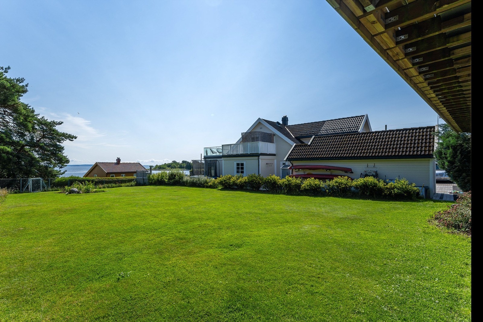 Deler av tomten er inngjerdet med flettverksgjerde og i enden av hagen er det en port som leder videre ned til kyststien og strandområdet. Galleribilde