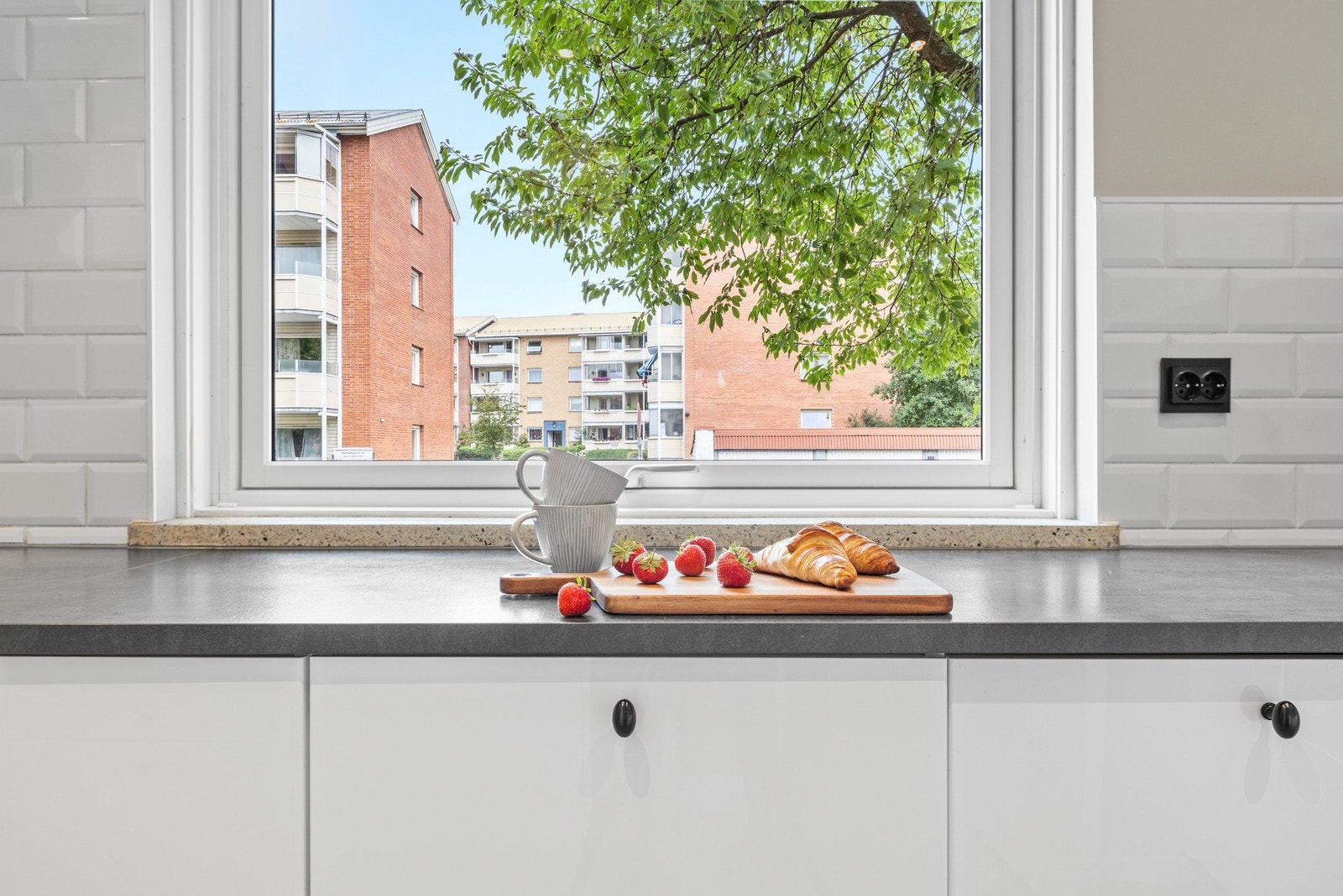 Kjøkkenet fremstår moderne med hvite overflater og integrerte hvitevarer Galleribilde