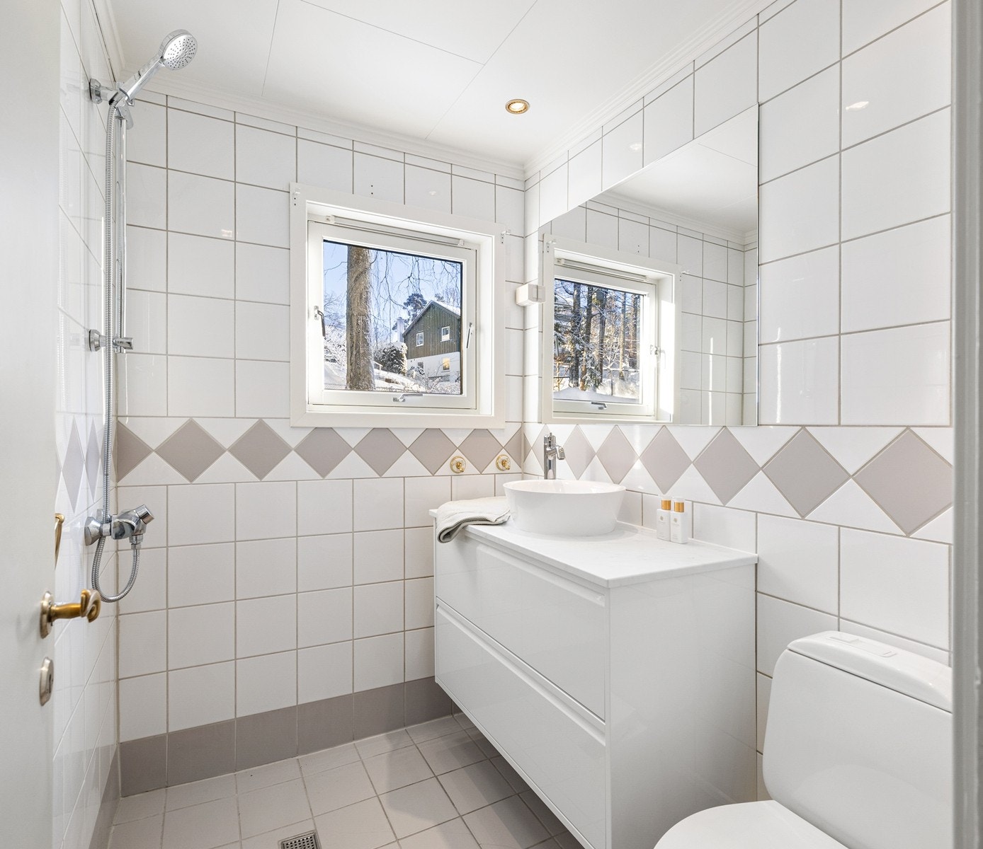 Flislagt baderom med vindu og downlights i himling. Innredningen består av et underskap, servant, speil, stikk og en dusjsone med dusjing direkte på gulv og vegg. Galleribilde
