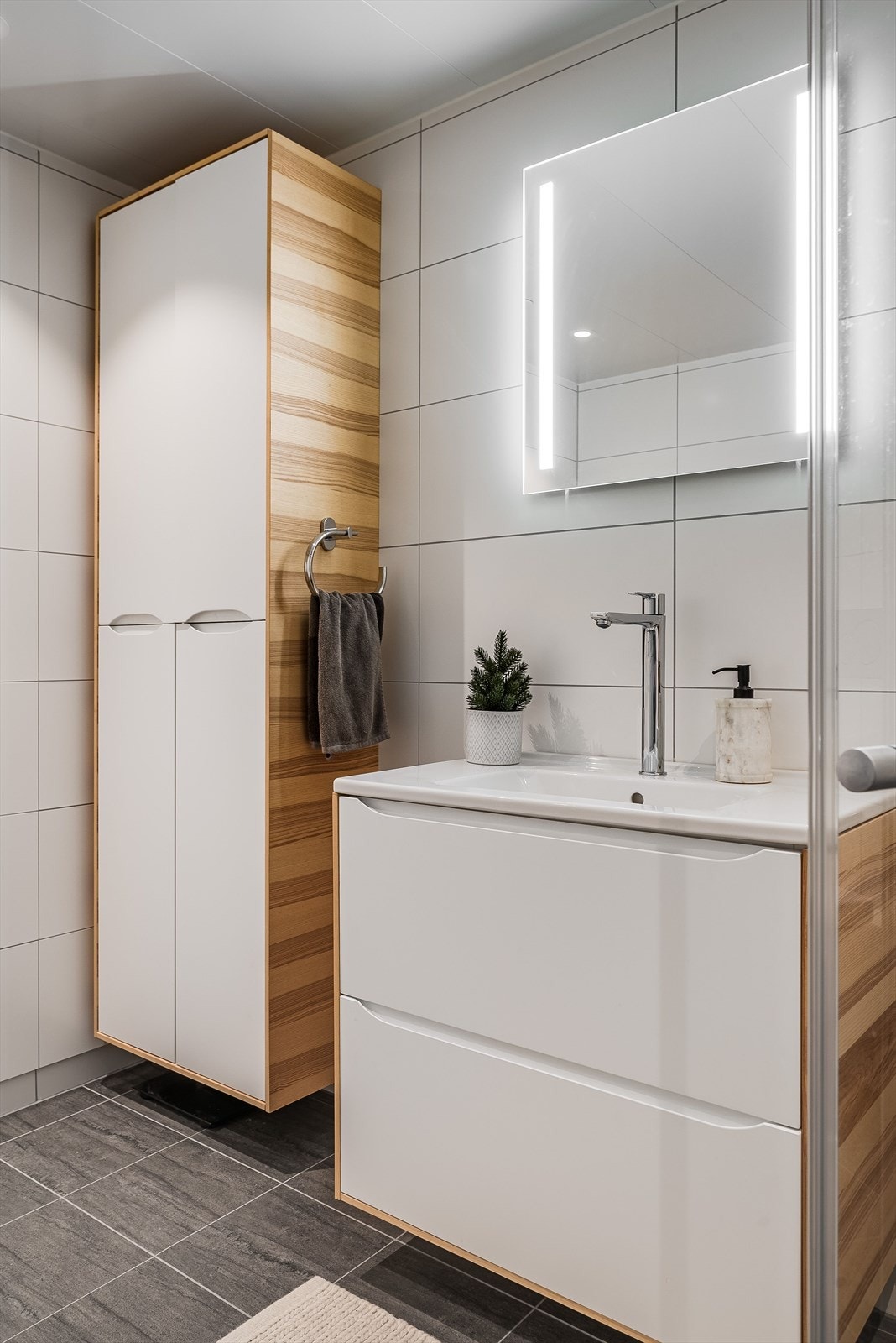 Badet har vegghengt servantinnredning med ovenpåliggende servant og speil med belysning, vegghengt høyskap, dusjhjørne med glassdører, vegghengt toalett og opplegg for vaskemaskin. Galleribilde