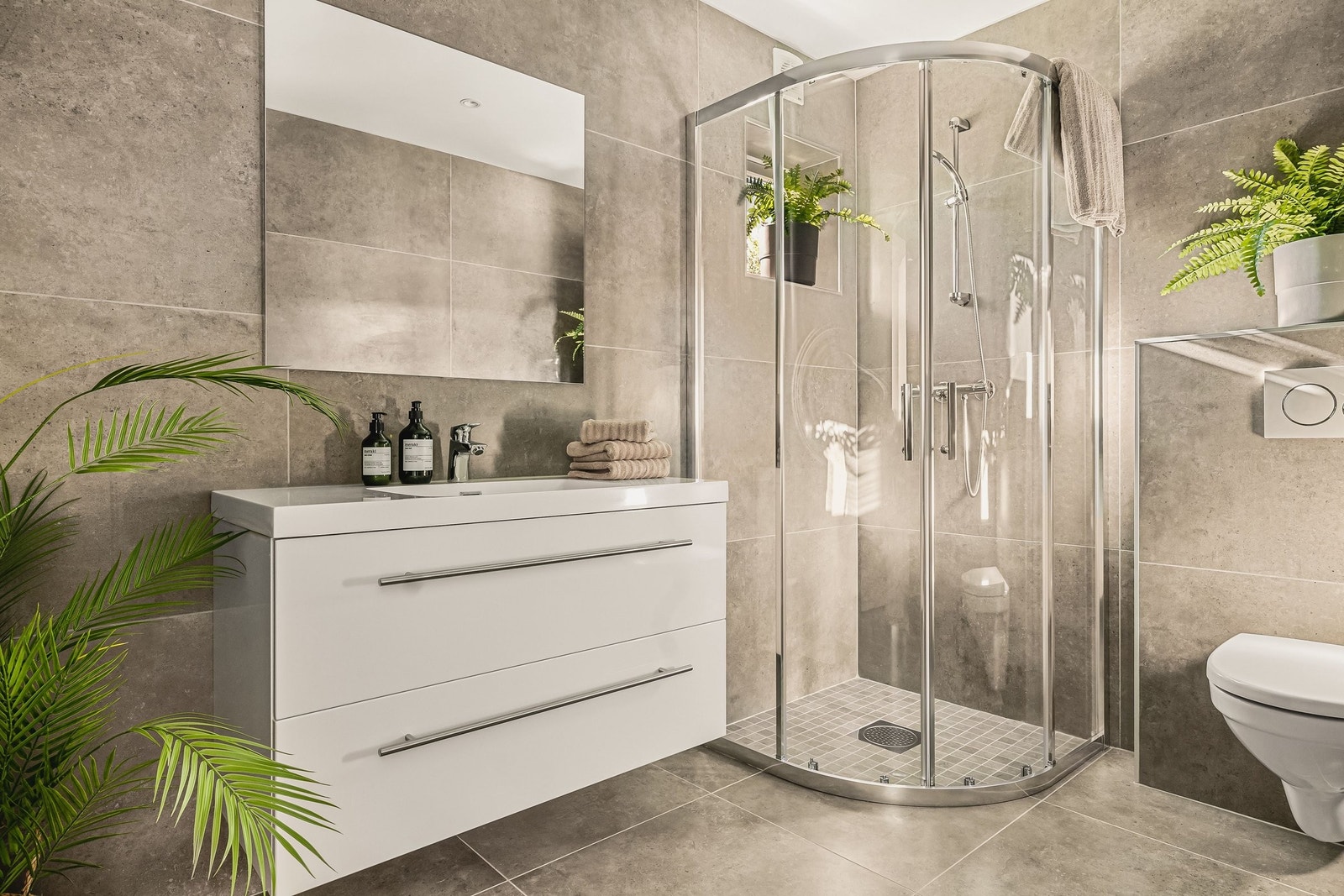 Badet er fra 2020 og er lekkert helfliset med gulvvarme. Det inneholder dusjhjørne, benkeskap med servant og vegghengt toalett. Galleribilde