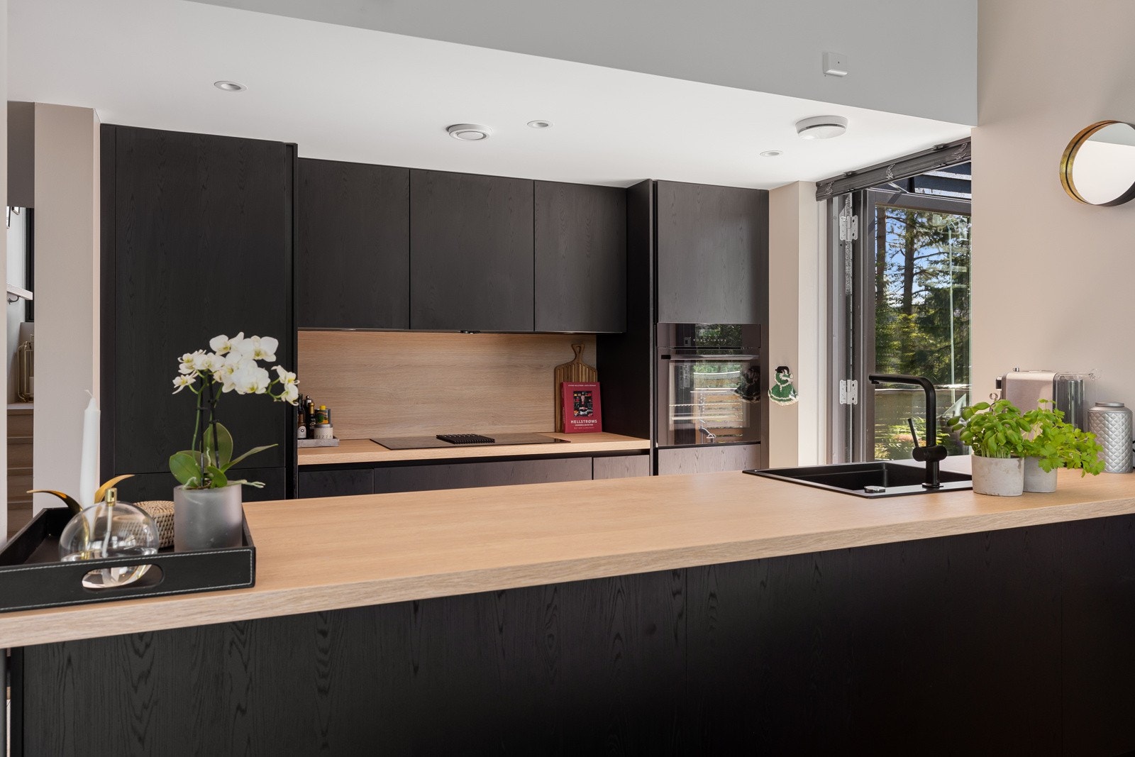 Et stilrent, sosialt og lekkert innredet kjøkken med stor kjøkkenøy og integrerte hvitevarer og ventilator. Galleribilde