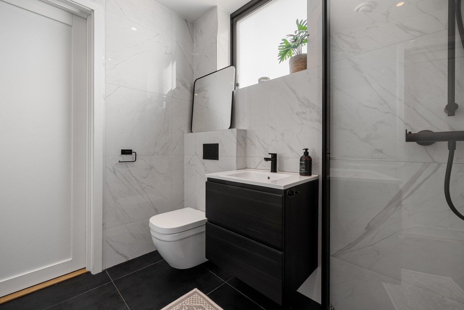 Det er lekre, moderne fliser på gulv, dels flislagte og malte vegger, downlights i tak og stilren baderomsinnredning. Galleribilde