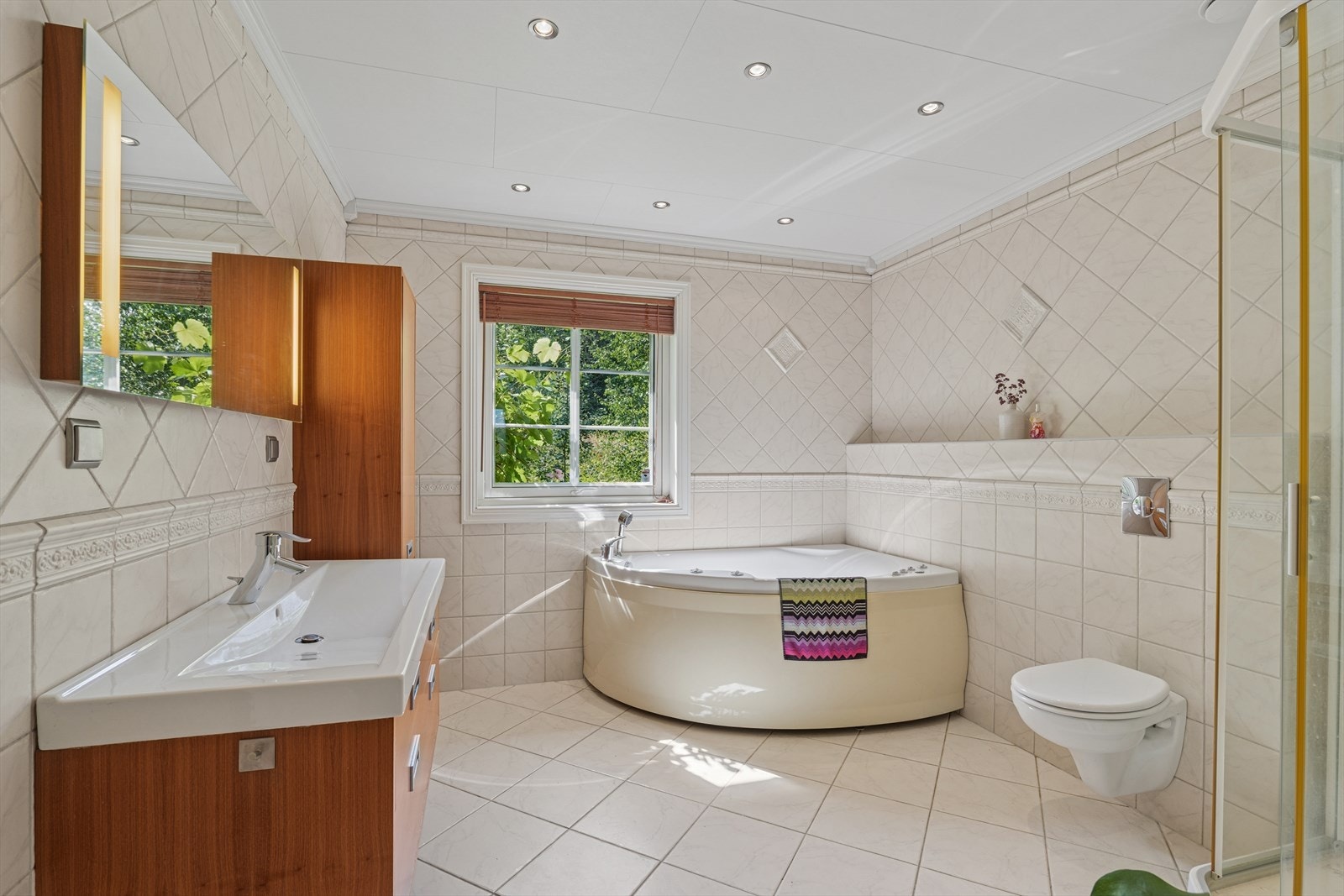 Her finner du en stor hjørnebadekar som inviterer til avslapning, samt en praktisk dusjløsning med glassdører. Galleribilde