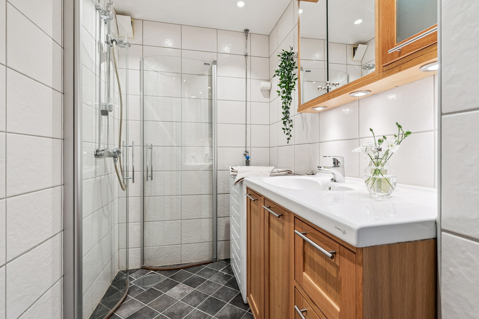 Baderommet er utstyrt med varmekabler i gulv og downlights i himling, samt dusj med inn / utadslående dusjvegger, servant med underskap, overskap med speilfronter og overlys, veggskap og opplegg for vaskemaskin. Vaskemaskin medfølger. Galleribilde