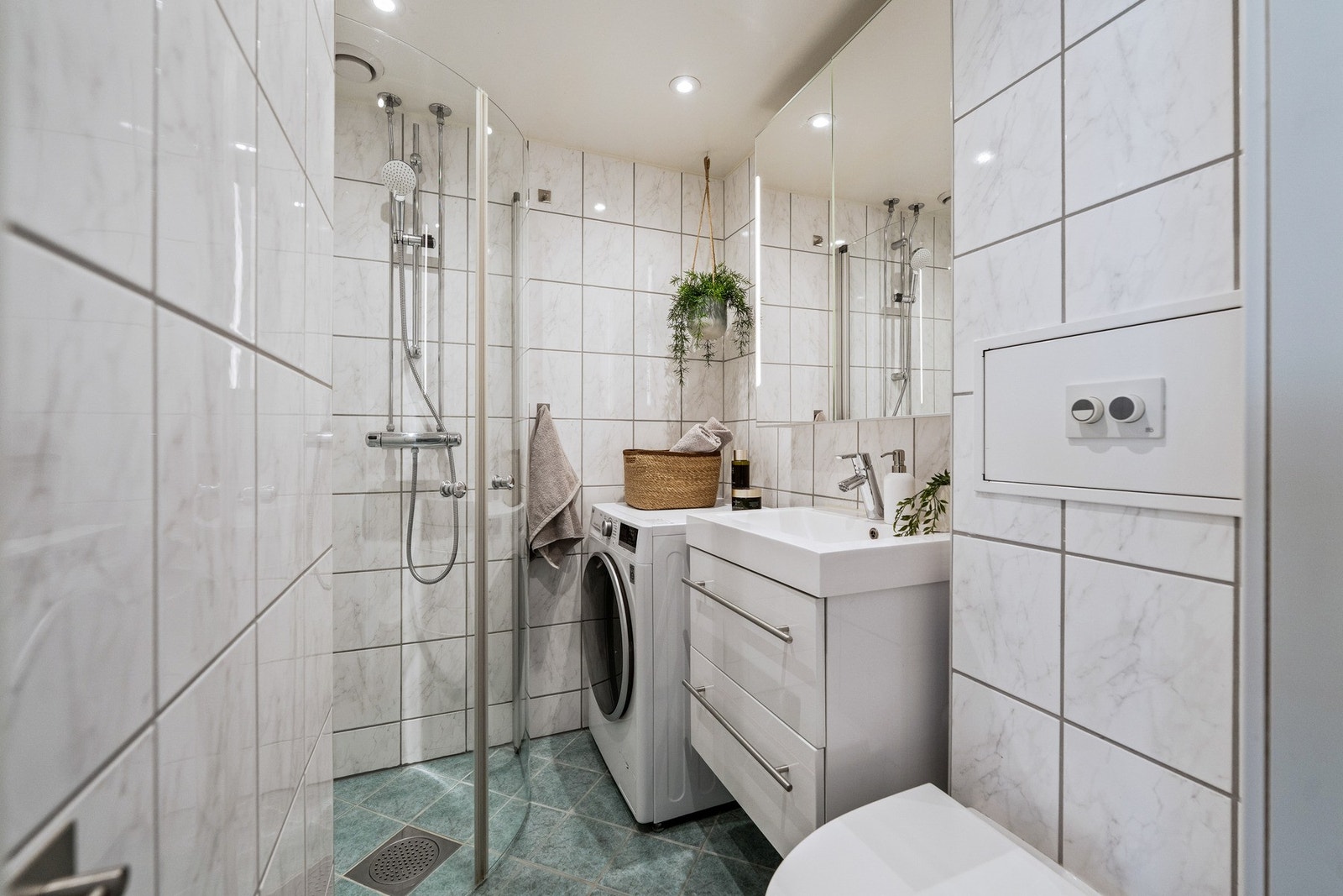 Effektivt bad med stilrene fliser, downlights i himling, dusjhjørne med glassdører og vegghengt toalett. Galleribilde