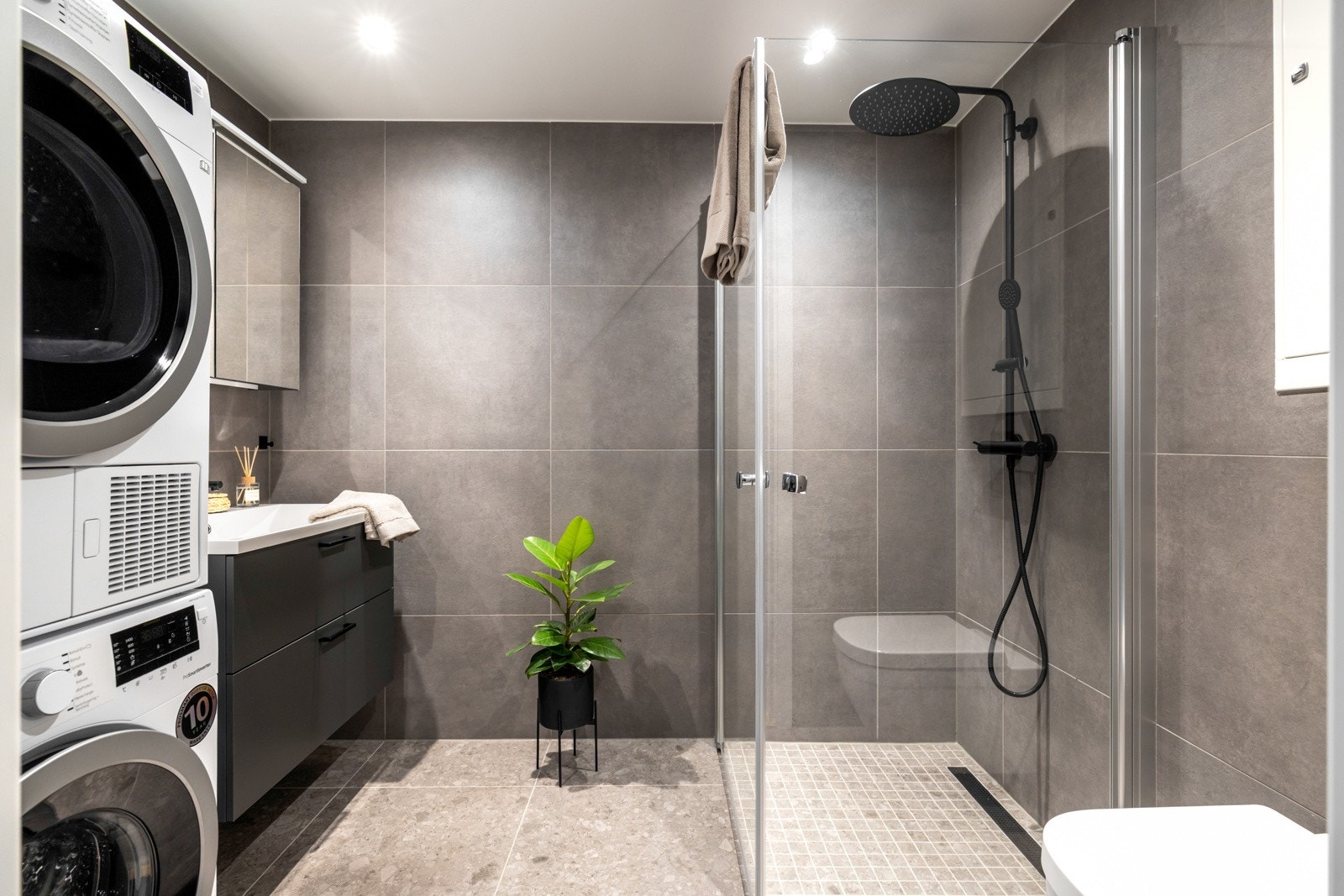 Badet er flislagt med moderne og stilrene overflater og utstyrt med vegghengt toalett, dusjhjørne med glassdører, servant med underskap og speilskap over. Galleribilde