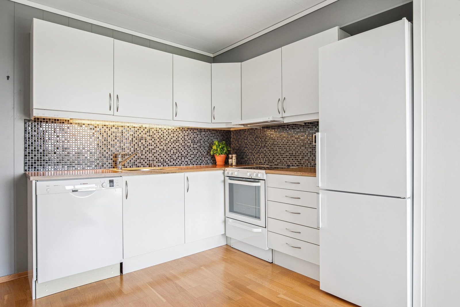 Pent kjøkken med tidløse fronter, flislagt mellom benk og overskap, og godt med oppbevaringsplass både oppe og nede. Galleribilde