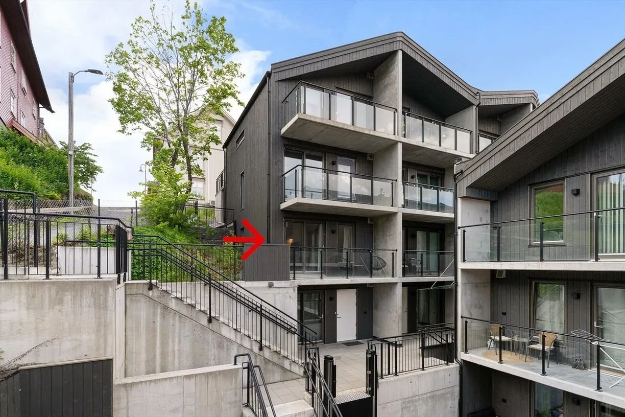 Moderne og stilren bygård med gjennomført arkitektur og gode solforhold – leiligheten (markert med rød pil) ligger i byggets første etasje med usjenert uteplass og enkel adkomst via trapp. Galleribilde