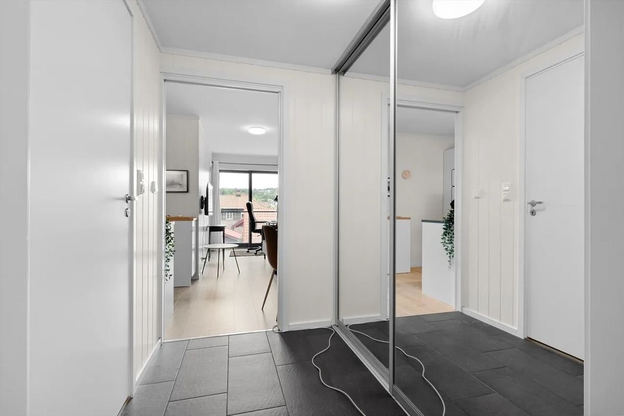 Lys og innbydende entré med praktisk flislagt gulv og stor skyvedørsgarderobe med speil – gir godt med oppbevaringsplass og et luftig førsteinntrykk. Fin flyt videre inn til både kjøkken og stue. Galleribilde
