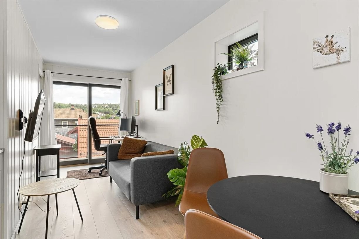 Lys og luftig stue med store vindusflater og utgang til balkong – rommet har en praktisk planløsning som gir plass til både sofakrok, hjemmekontor og underholdning. Galleribilde